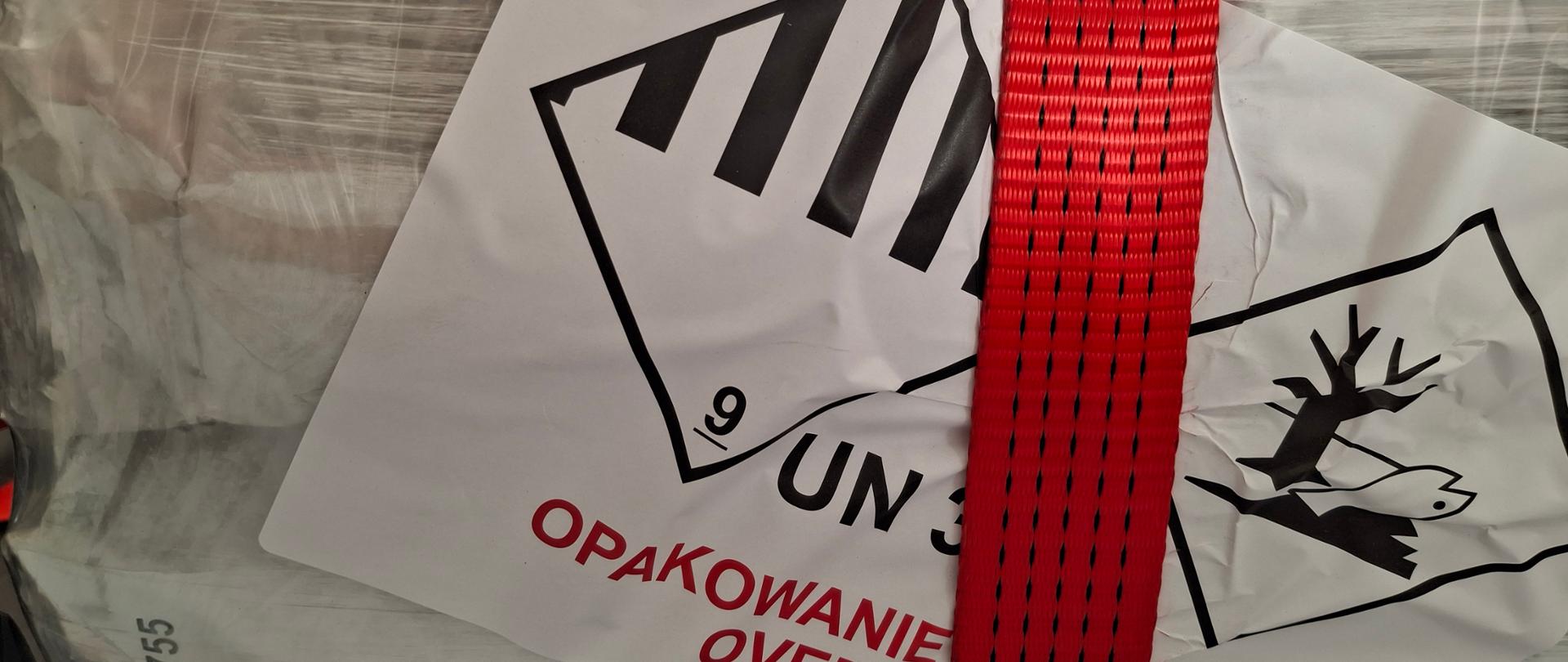 Etykieta ADR klasy 9 z oznaczeniem substancji niebezpiecznej dla środowiska umieszczona na opakowaniu typu big bag zabezpieczonym czerwonym pasem transportowym.