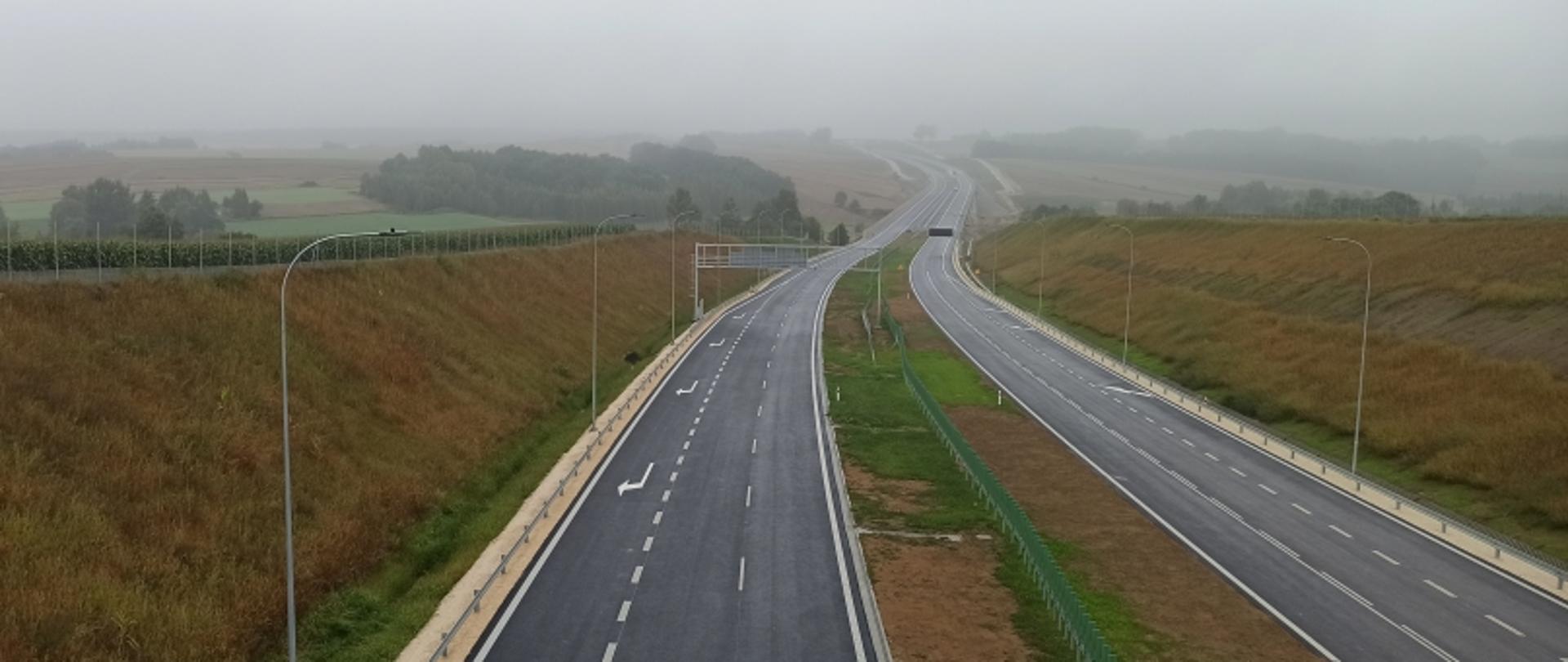 Pusta droga ekspresowa z dwoma pasami w każdą stronę, zielonym pasem pośrodku i zamglonym krajobrazem w tle.