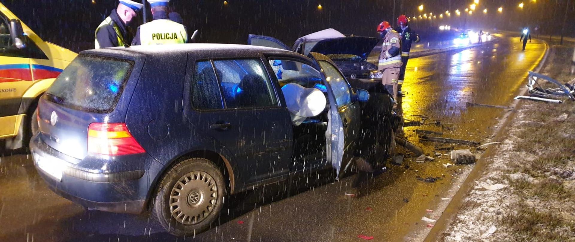 Rozbity samochód na drodze, obok policja i strażacy