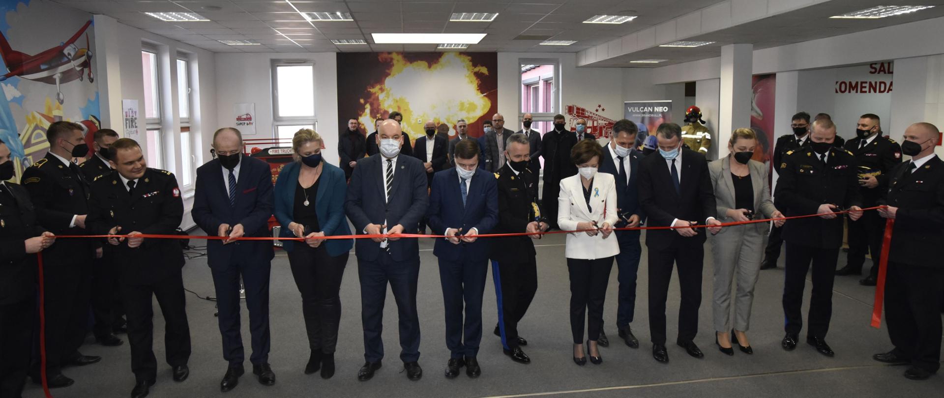 grupa kobiet i mężczyzn przecina czerwoną wstażkę, w tle ludzie 