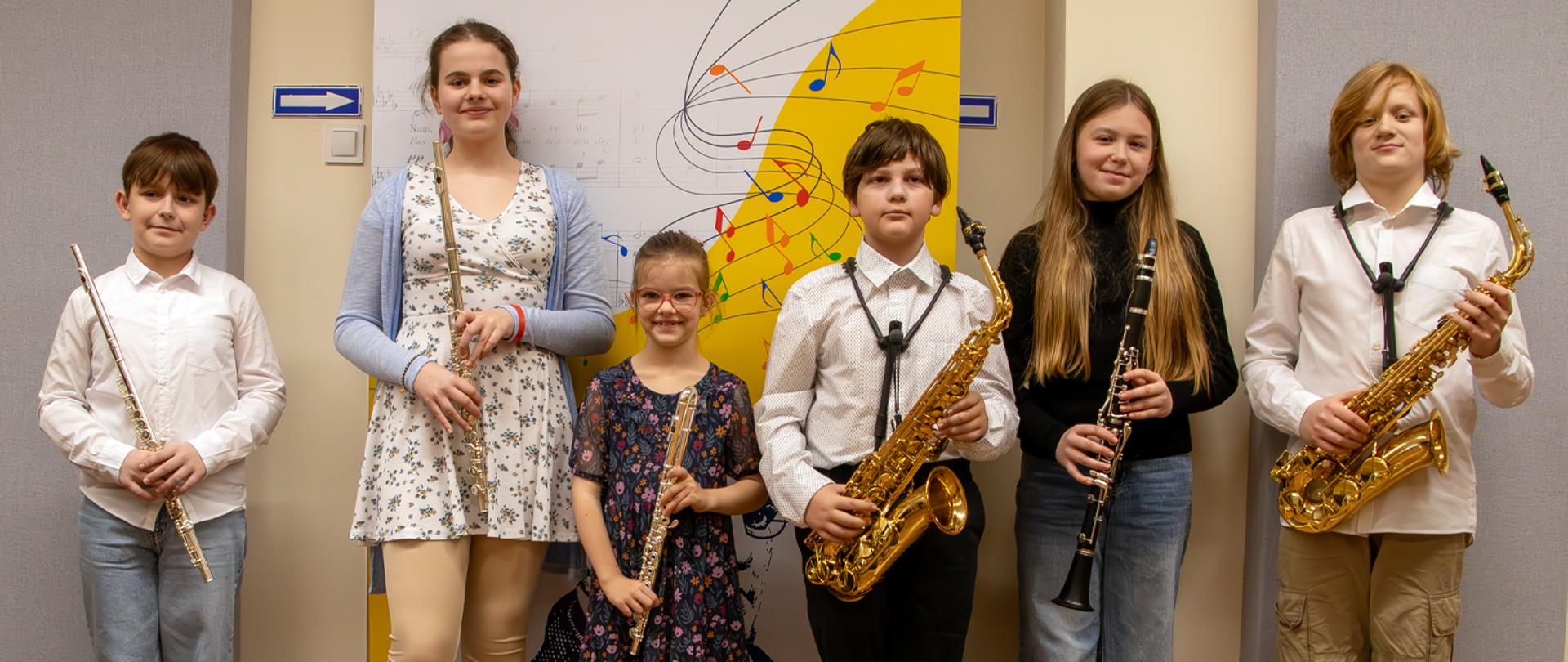 Na zdjęciu stoi sześcioro dzieci, trzymają w rękach flety, saksofony i klarnet.