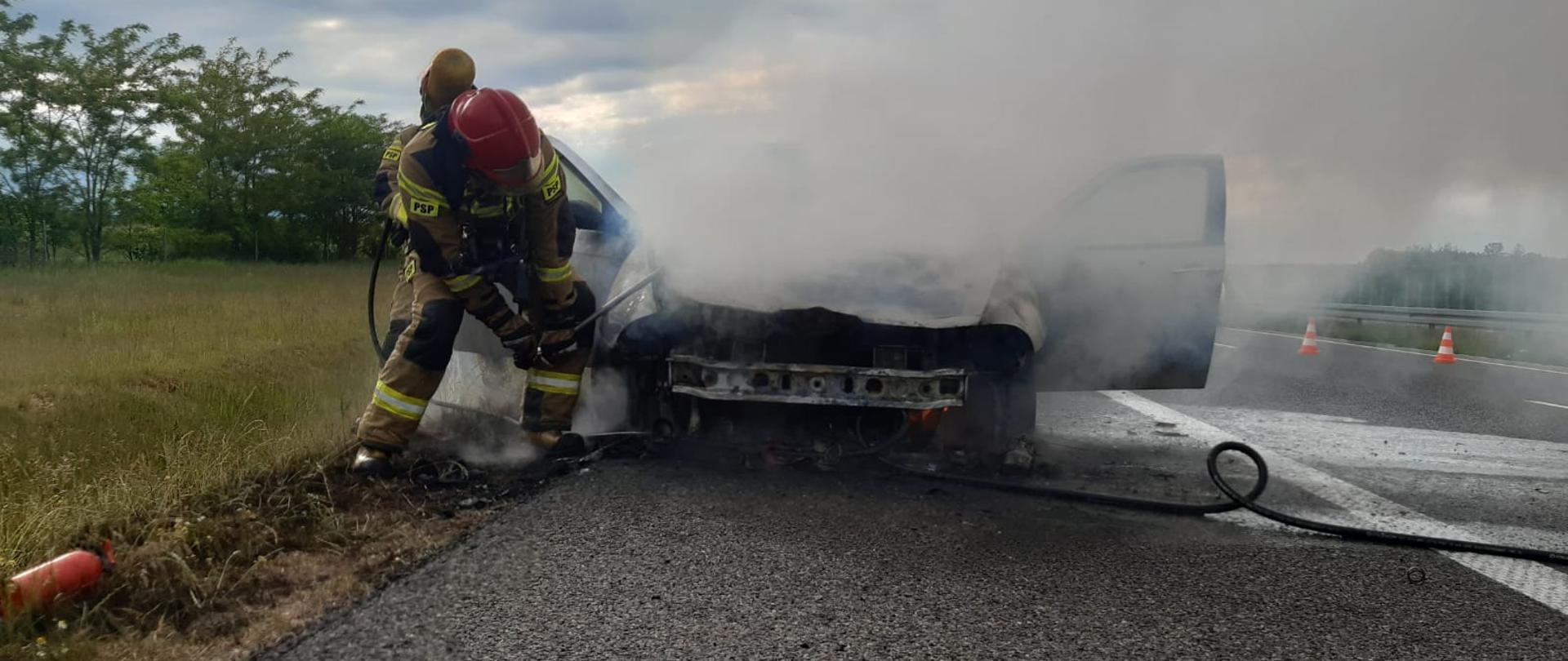Zdjęcie przedstawia strażaka gaszącego samochód.