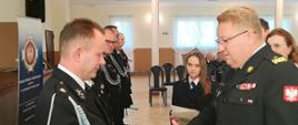 Komendant Wojewódzki PSP wręcza promesę członkowi OSP. Wyciąga rękę – gratuluje.