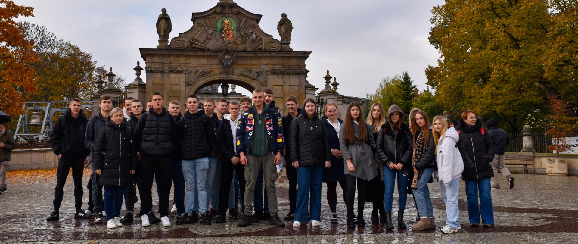 Grupa młodzieży z opiekunami stoi pod bramą na Jasną Górę