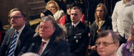 Zastępca Komendanta Centralnej Szkoły PSP siedzący podczas mszy, wokół inni wierni