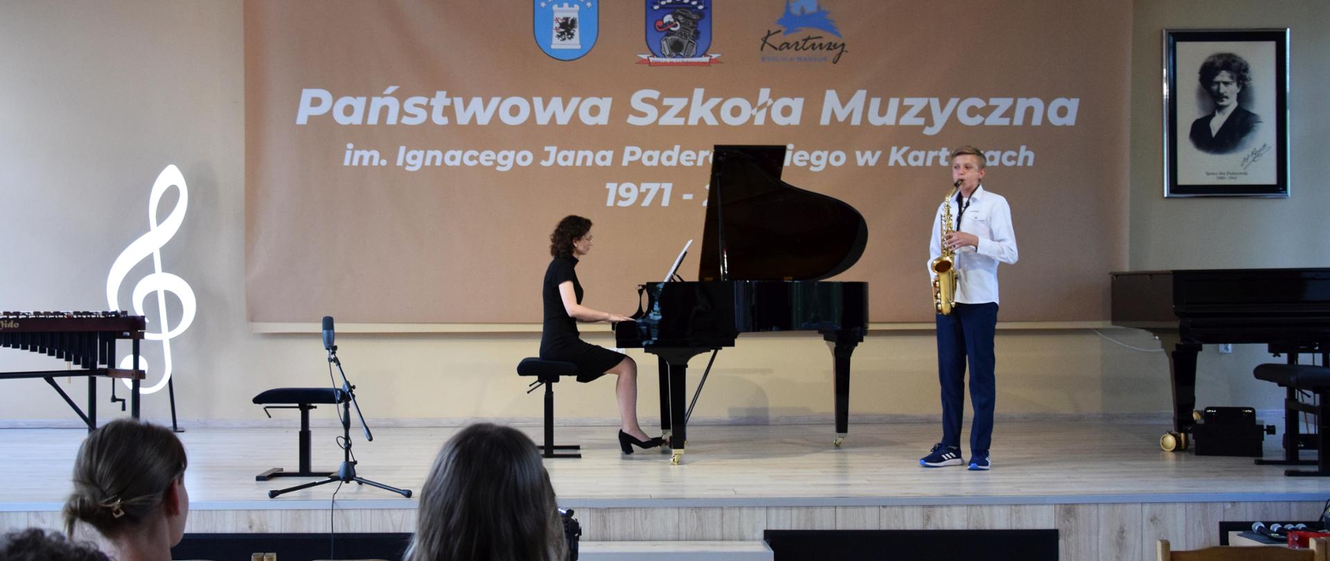 na scenie gra saksofonista i akompaniatorka, częściowo widoczni są słuchacze