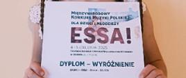 Na zdjęciu jest uczennica trzymająca dyplom z wyróżnieniem za Międzynarodowy konkurs Muzyki Polskiej dla dzieci i młodzieży ESSA!