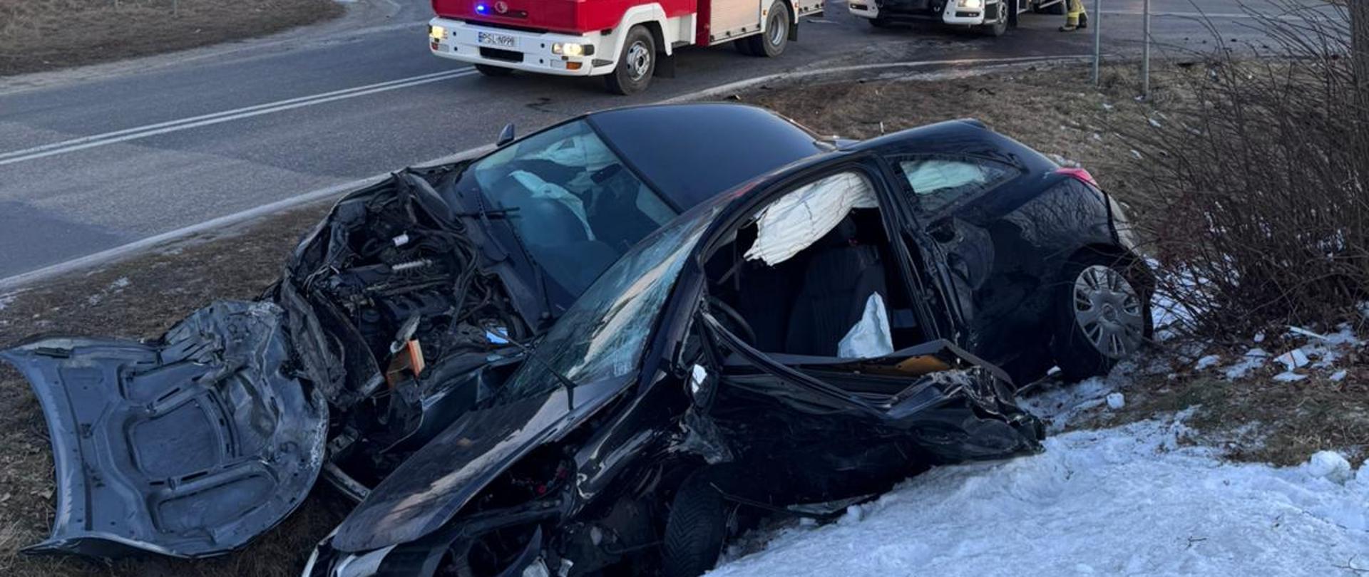 Uszkodzone samochody w przydrożnym rowie za nimi samochody ratownicze