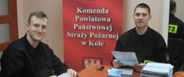 Zdjęcie przedstawia dwóch strażaków przygotowujących ulotki zachęcające do szczepienia się przeciwko COVID-19