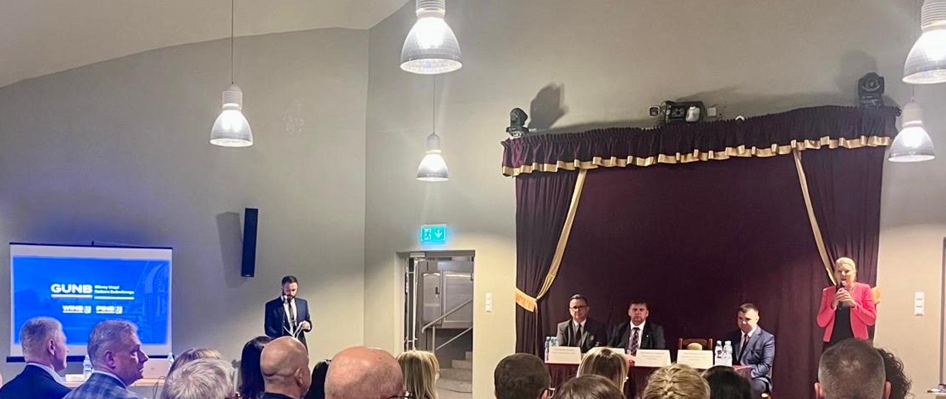 Narada szkoleniowa nadzoru budowlanego województwa świętokrzyskiego z udziałem przedstawicieli Głównego Urzędu Nadzoru Budowlanego (GUNB). Uczestnicy siedzą na sali konferencyjnej, przed nimi prelegenci przy stole oraz prezentacja multimedialna.