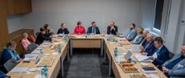 Widok od tyłu sali, za ustawionymi w czworokąt stołami siedzą ludzie, u szczytu stołu minister Kulasek i wiceminister Zioło-Pużuk.