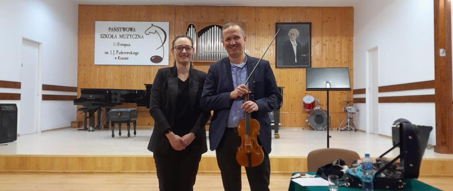Prowadzący z organizatorem stoją na scenie PSM w Koninie, w ręku trzyma skrzypce.