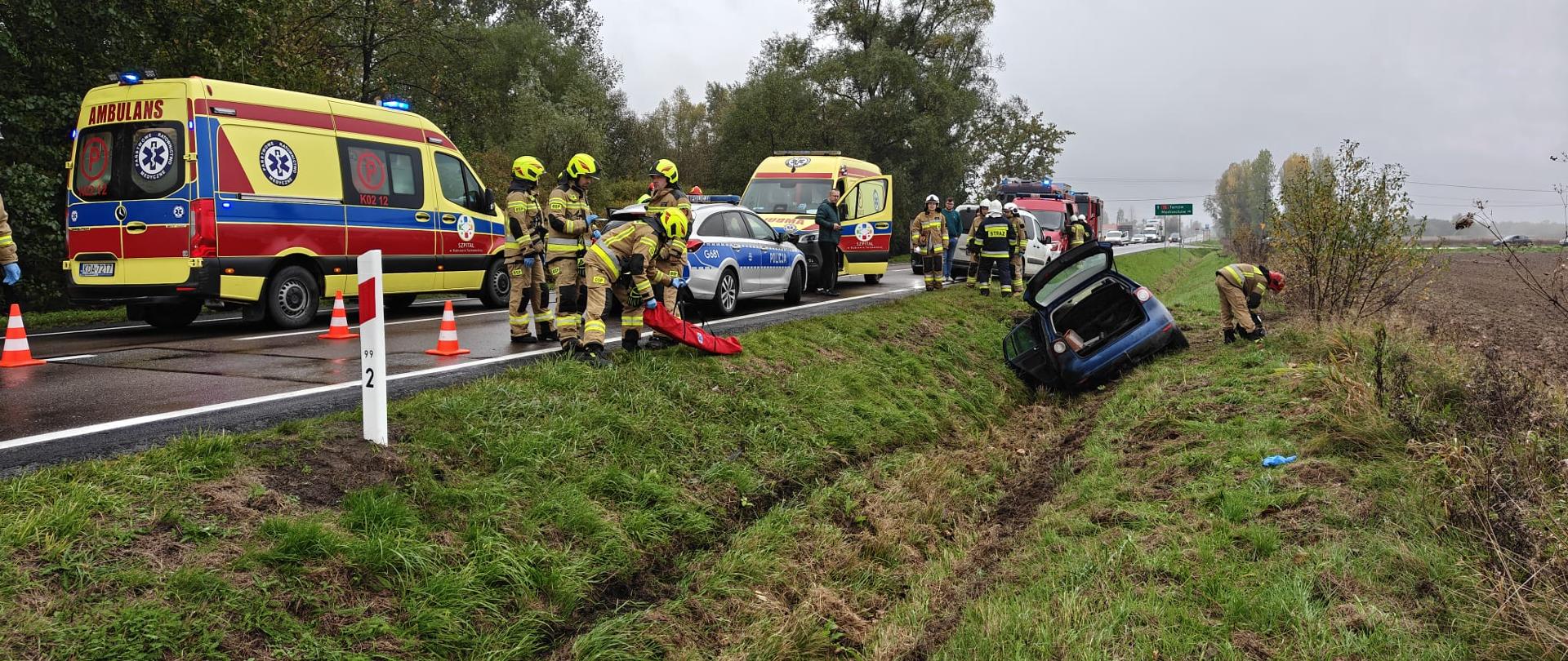 Na zdjęciu widać wypadek sam. osobowego który zjechał z drogi i uderzył w mostek, 2 Karetki Pogotowie Ratunkowego, patrol Policji, strażaków OSP i PSP udzielających pomocy oraz wozy strażackie.