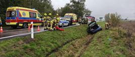 Na zdjęciu widać wypadek sam. osobowego który zjechał z drogi i uderzył w mostek, 2 Karetki Pogotowie Ratunkowego, patrol Policji, strażaków OSP i PSP udzielających pomocy oraz wozy strażackie.