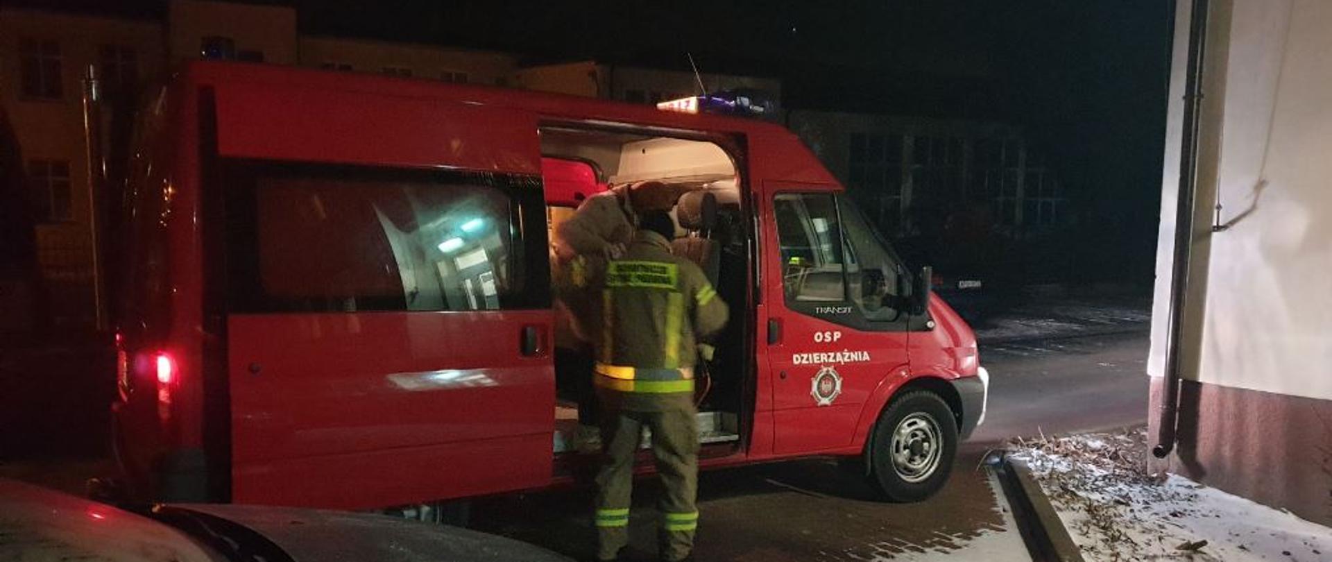 Samochód pożarniczy, lekki. Strażak w ubraniu specjalnym pomaga wyjść osobie starszej z tego samochodu.