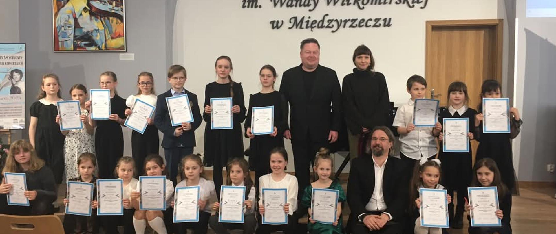 Jury w otoczeniu uczestników konkursu trzymających dyplomy.