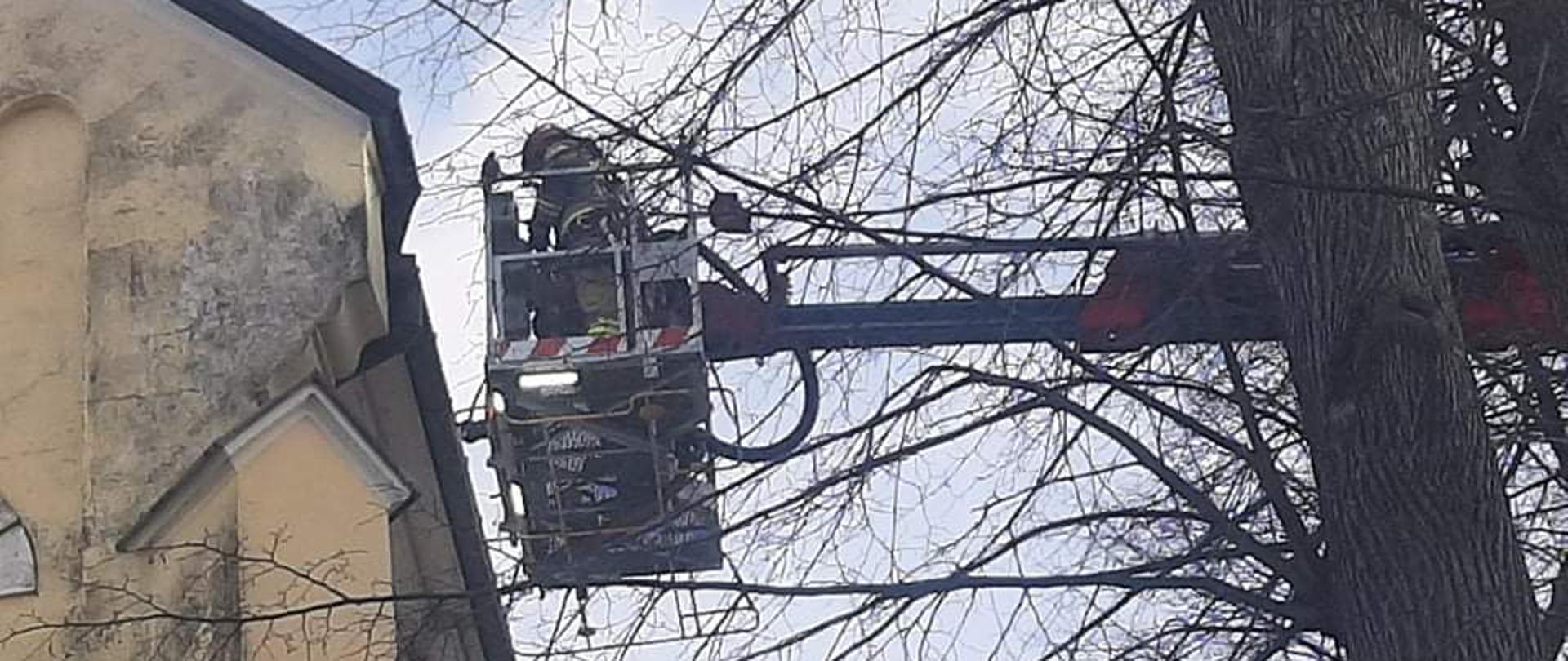 Strażacy w koszu . podnośnika zabezpieczają dach kościoła.