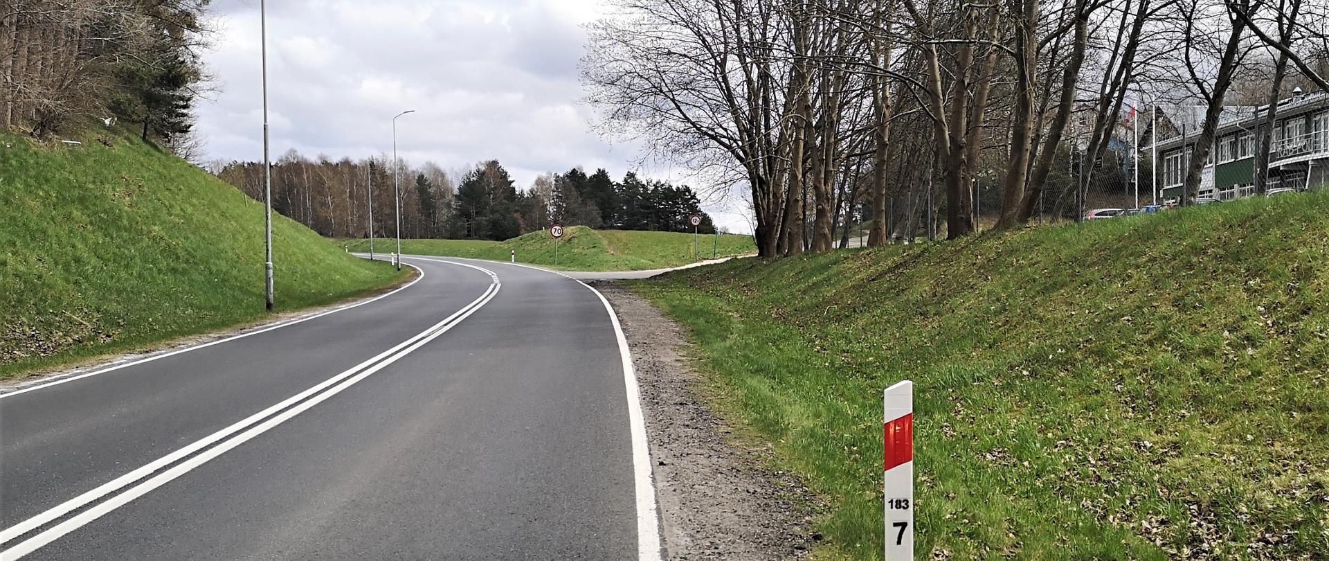 Zdjęcie przedstawia drogę krajową nr 20 w Przęsinie. Na pierwszym planie droga i pobocze, w oddali, po prawej budynki mieszkalne.