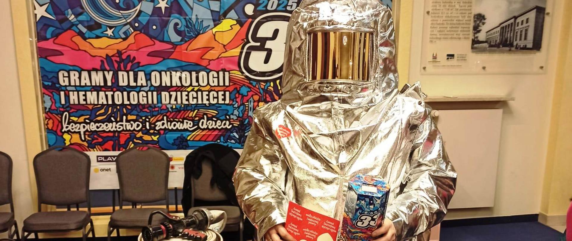 Zdjęcie przedstawia strażaka ubranego w ubranie ogniochronne. W tle widać baner WOŚP.