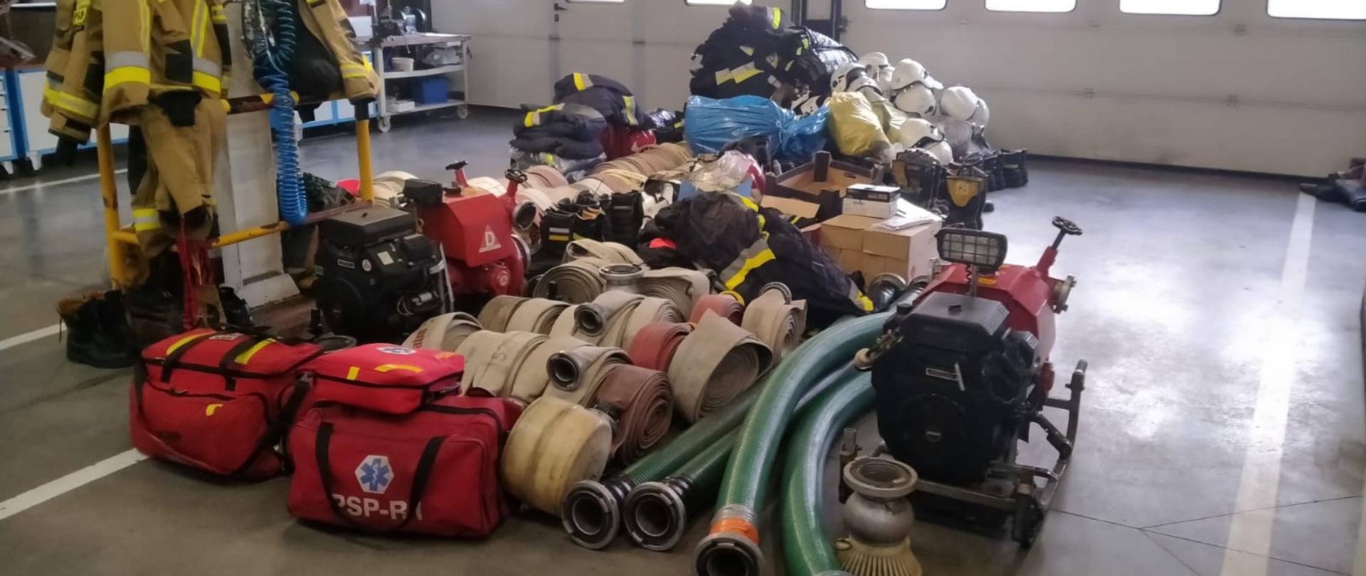 na zdjęciu widać zebrany w garażu sprzęt pożarniczy, motopompy, węże pożarnicze, torby medyczne, mundury hełmy itp.