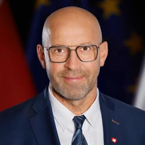 Minister Sportu i Turystyki Jakub Rutnicki stoi na tle flag Polski i Unii Europejskiej