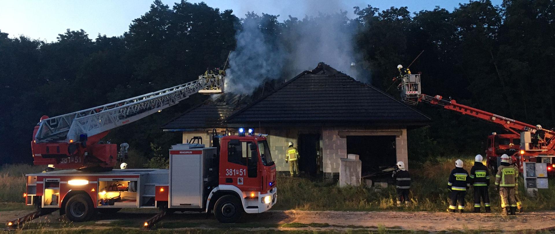 Dwie strażackie drabiny mechaniczne gaszą płonący budynek. 