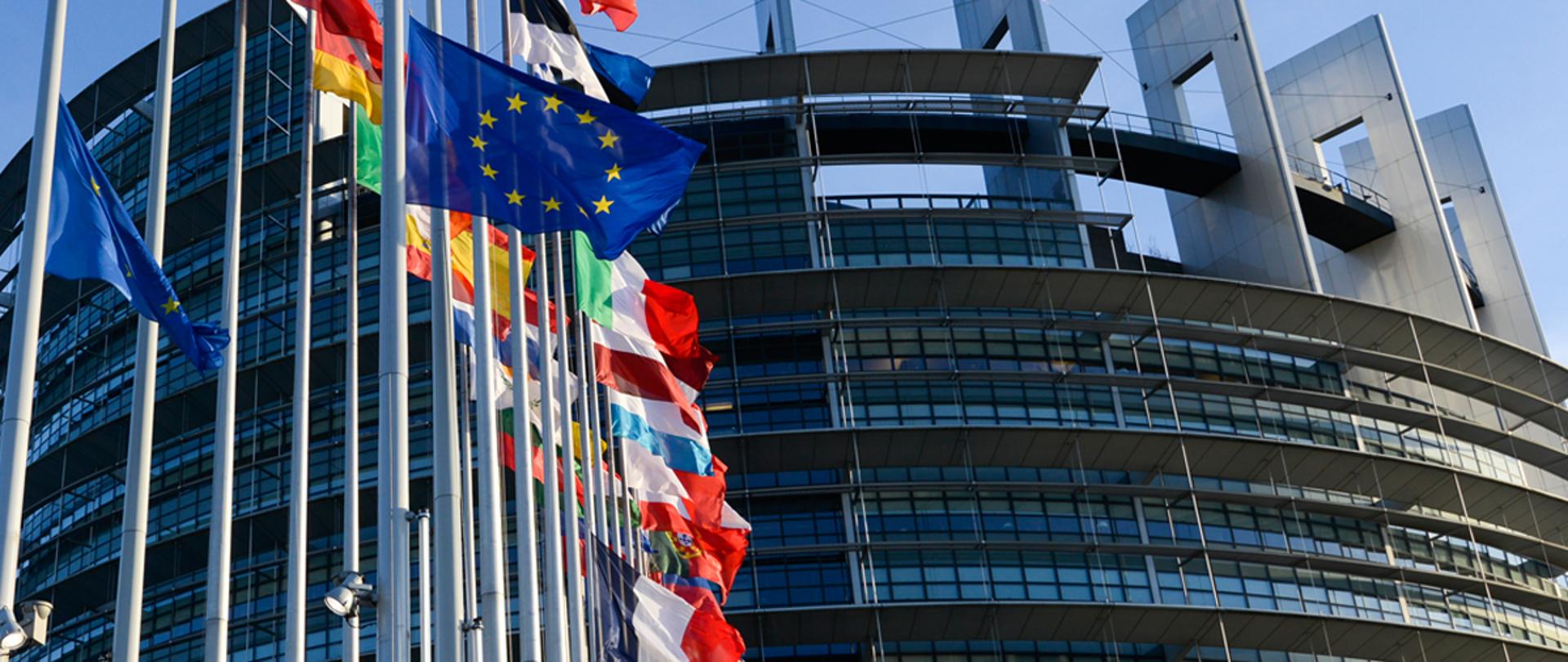 Flagi państwowe na tle budynku parlamentu europejskiego wzniesione na masztach