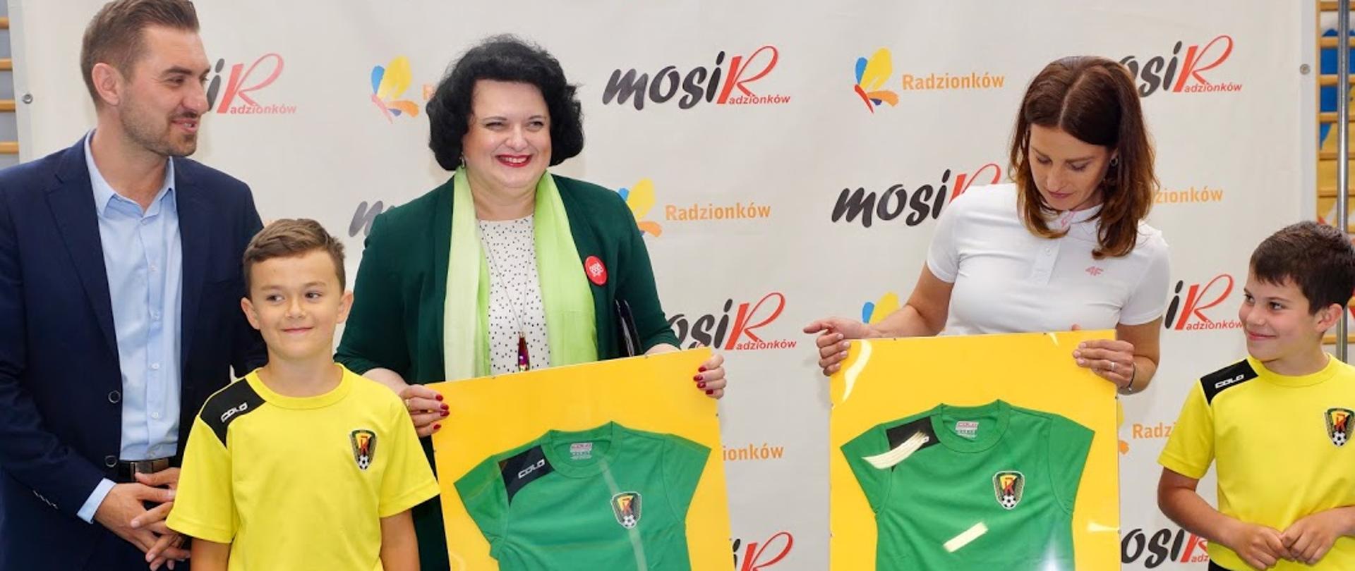 Minister Danuta Dmowska-Andrzejuk trzyma koszulkę klubu na grupowym zdjęciu.