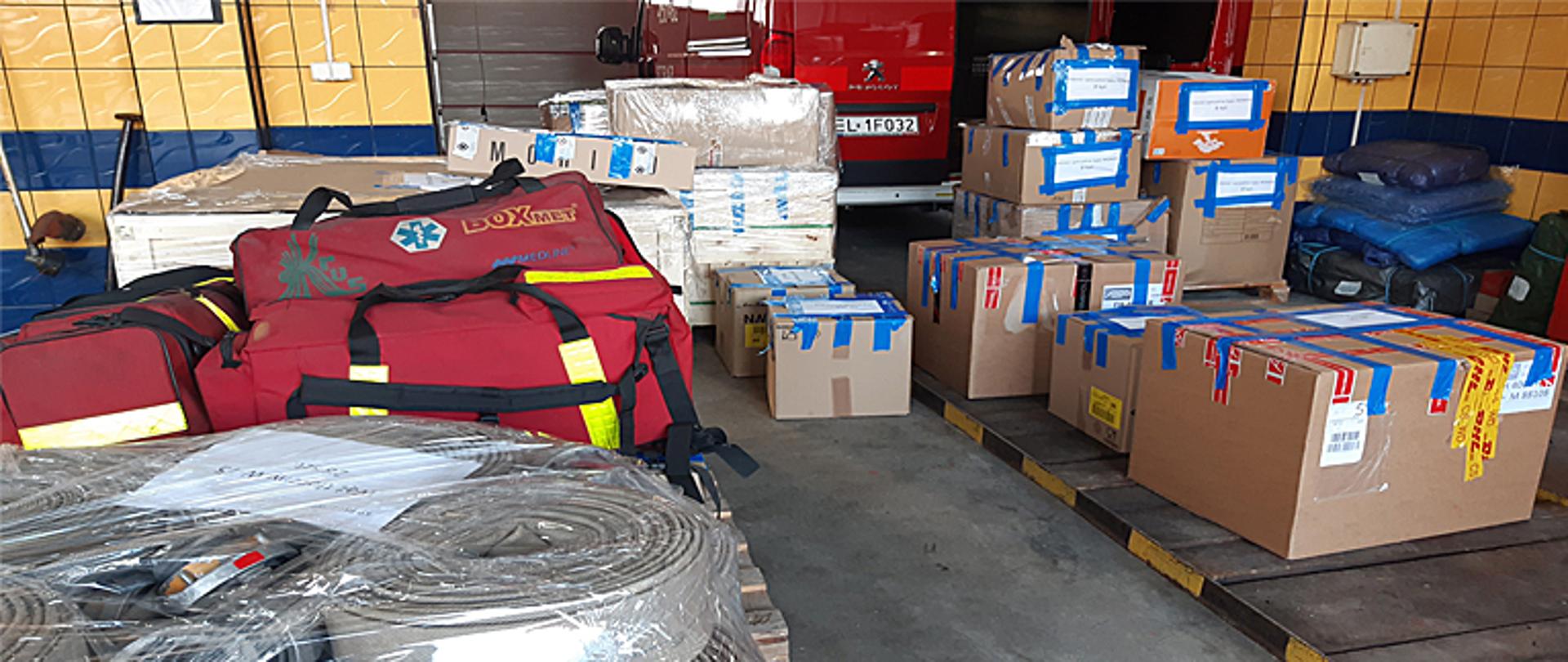 Kilkanaście pudeł kartonowych stojących na sobie leży na garażu, po lewej stronie trzy czerwone torby medyczne, na pierwszym planie węże strażackie w torbach foliowych