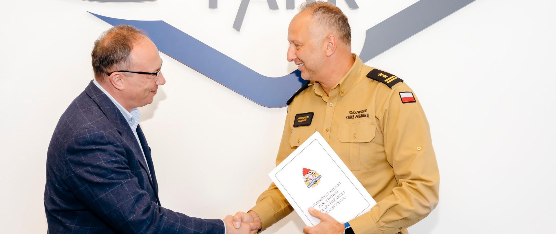Po lewej prezes Wałbrzyska Specjalna Strefa Ekonomiczna "INVEST-PARK" podaje rękę Komendantowi Miejskiemu Państwowej Straży Pożarnej w Wałbrzychu. Komendant trzyma w ręce białą teczkę