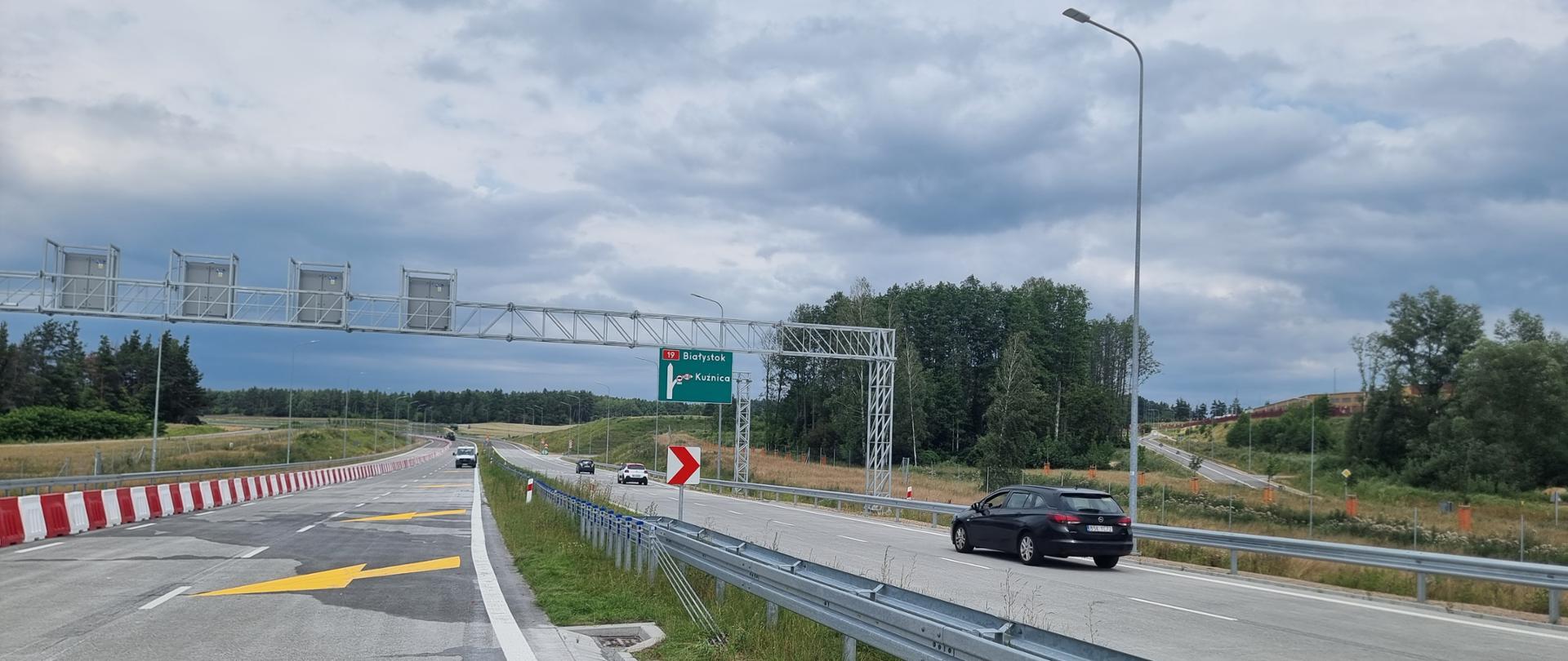 Dwie jezdnie, w środku pas rozdziału z barierą, na prawej jezdni trzy auta jedno za drugim