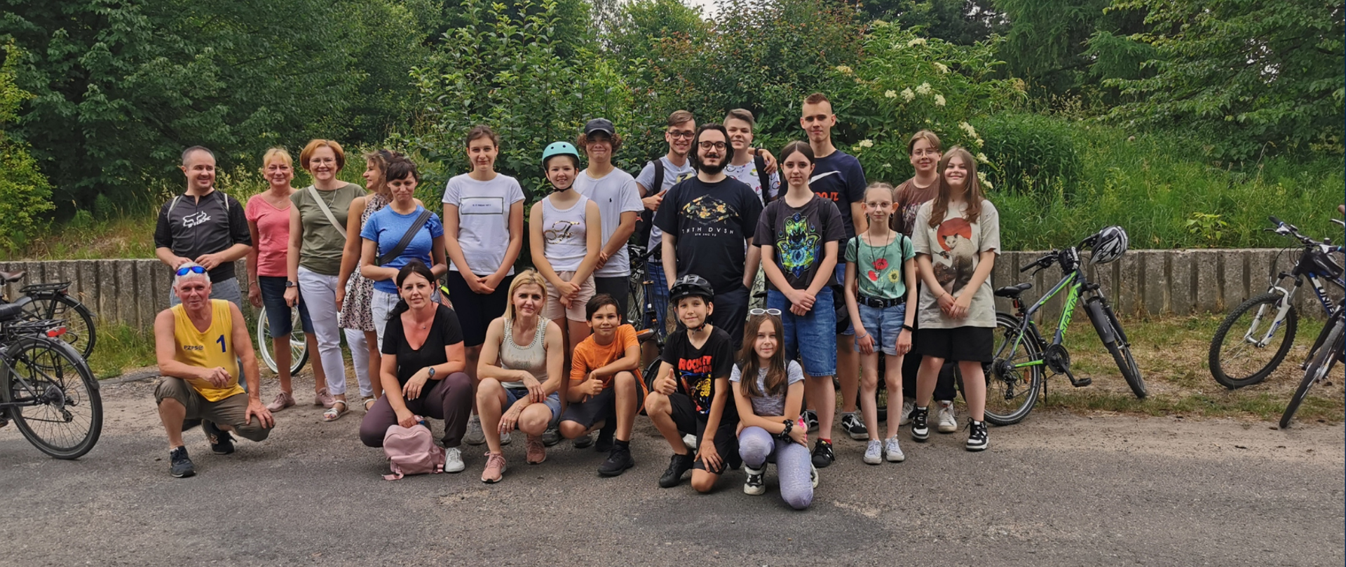 Zdjęcie przedstawia uczniów i nauczycieli, którzy brali udział w rajdzie rowerowym 21 czerwca 2023 roku. W tle zielone drzewa.