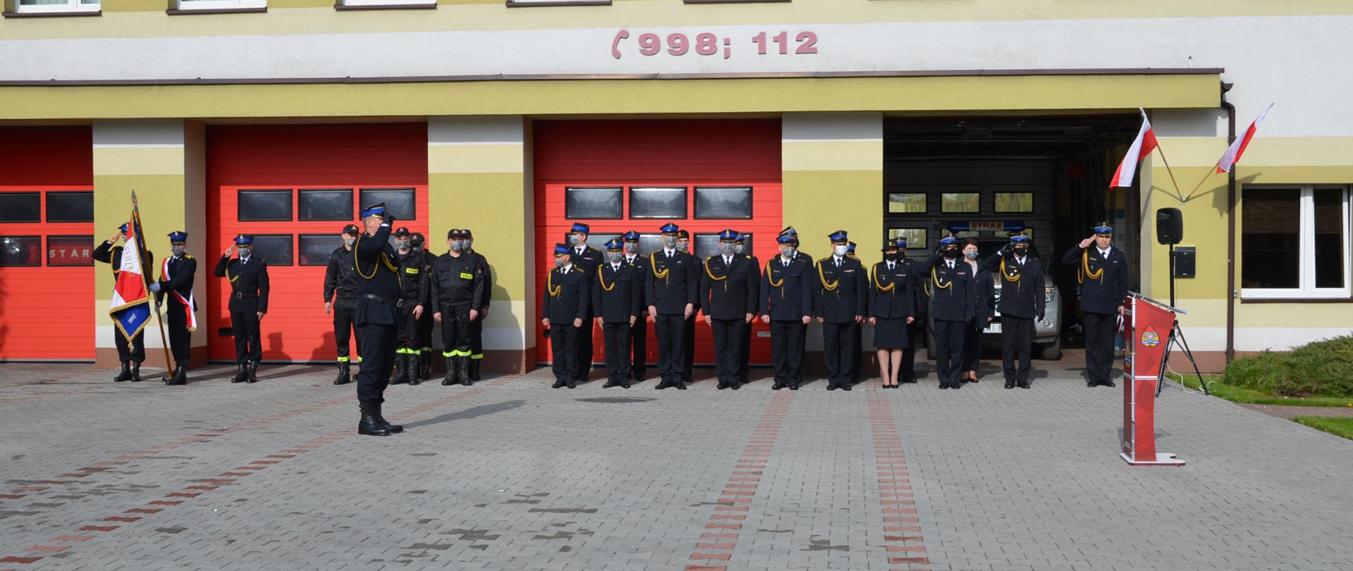 Zdjęcie przedstawia dowódcę uroczystości z pododdziałem strażaków i budynek strażnicy