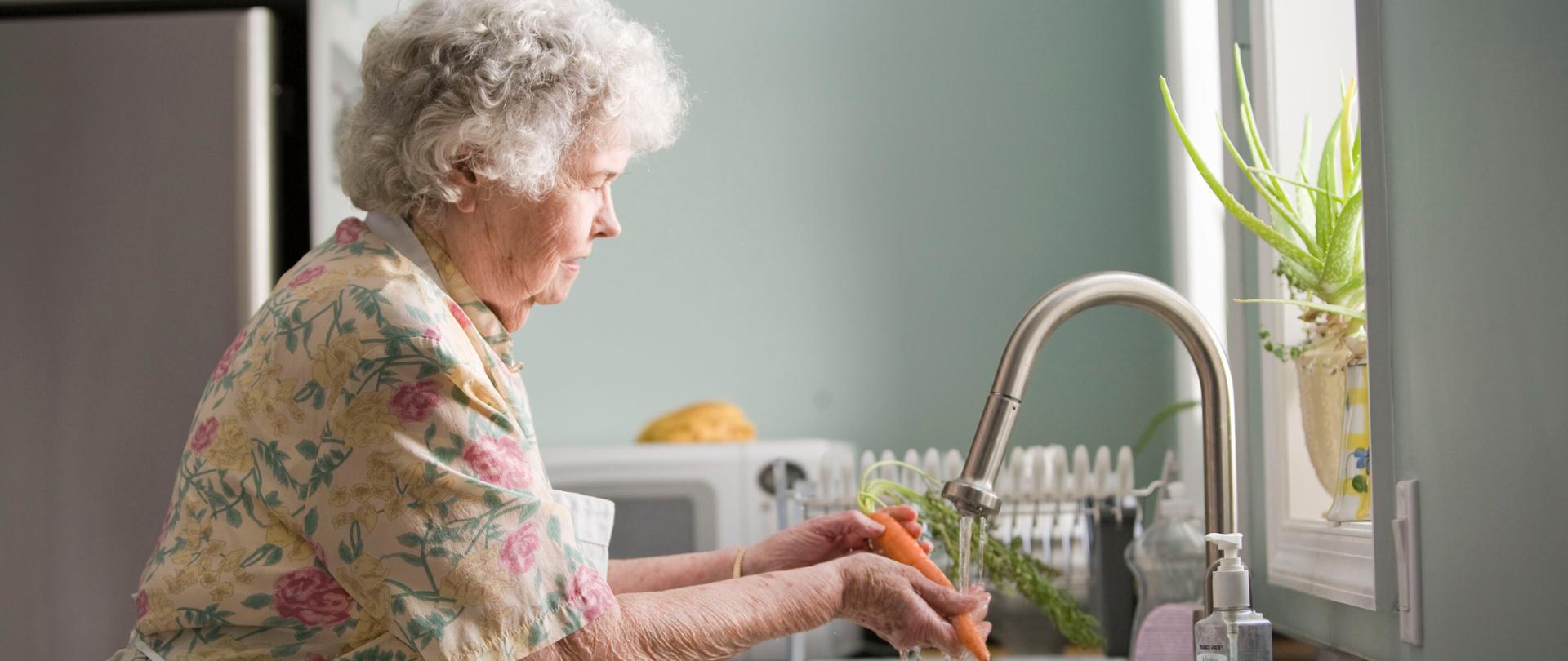 Starsza kobieta myje warzywa w kuchni