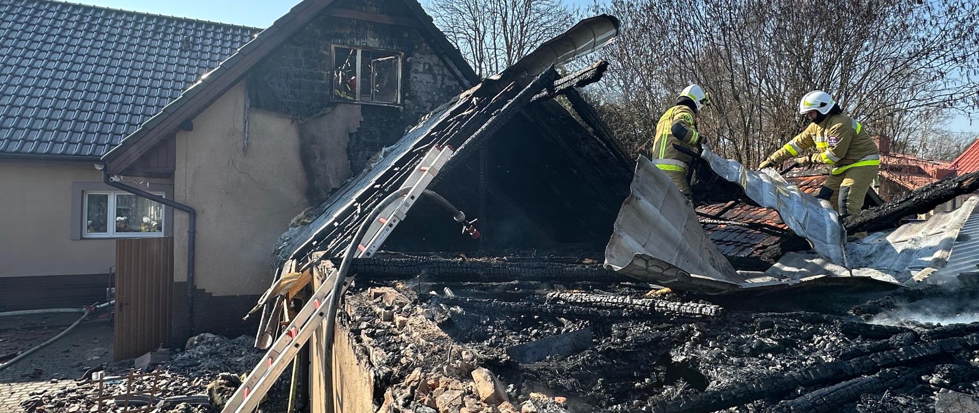Strażacy pracujący na dachu spalonego budynku gospodarczego.
