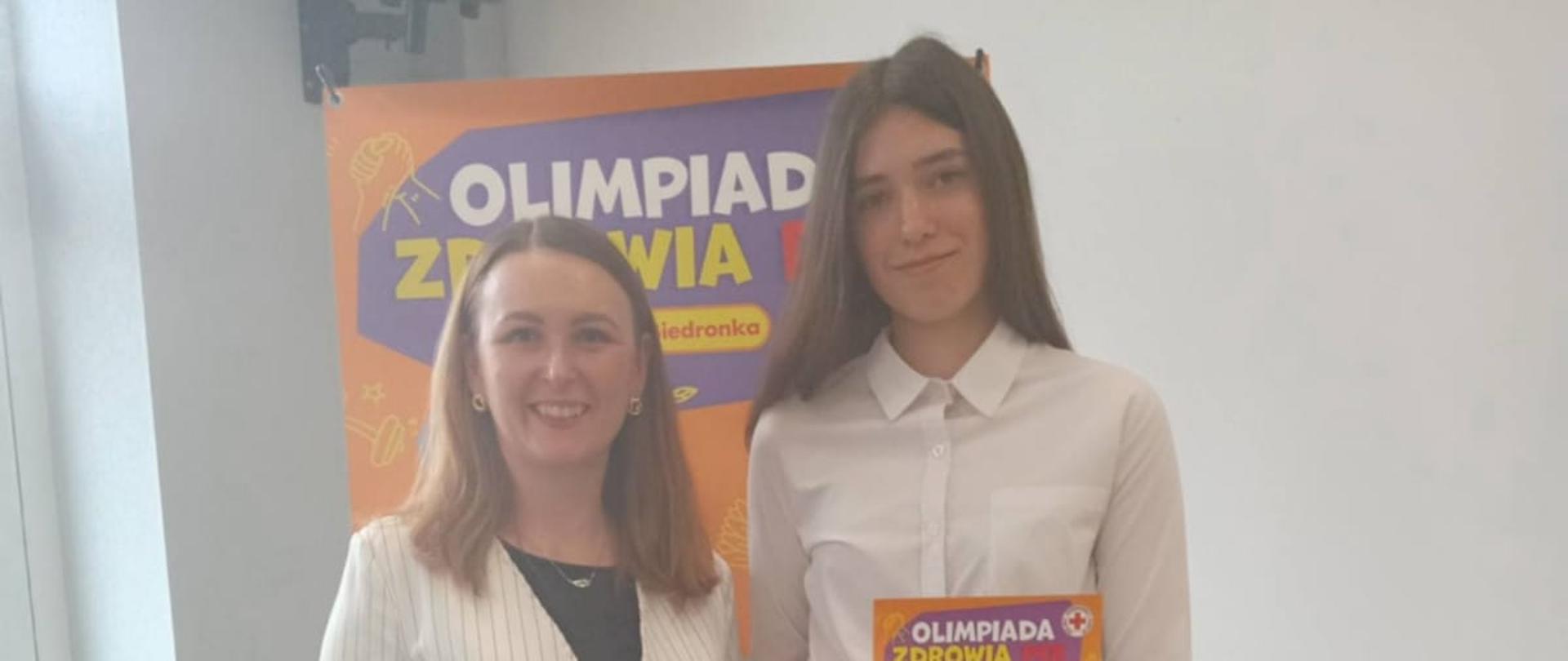 Uczennica ZSCKR z nauczycielką przed plakatem z nagrodą i dyplomem 