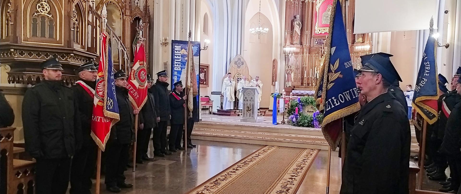 Poczty sztandarowe strażaków stoją w trakcie mszy. W tle widoczny ołtarz.