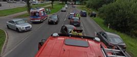 Widok na miejsce zdarzenia z góry. Zdjęcie wykonane z dachu pojazdu gaśniczego. Widać na nim drogę, rozbite pojazdy, duży ruch i pojazdy omijające strażaków. Na lewo widać karetkę pogotowia.