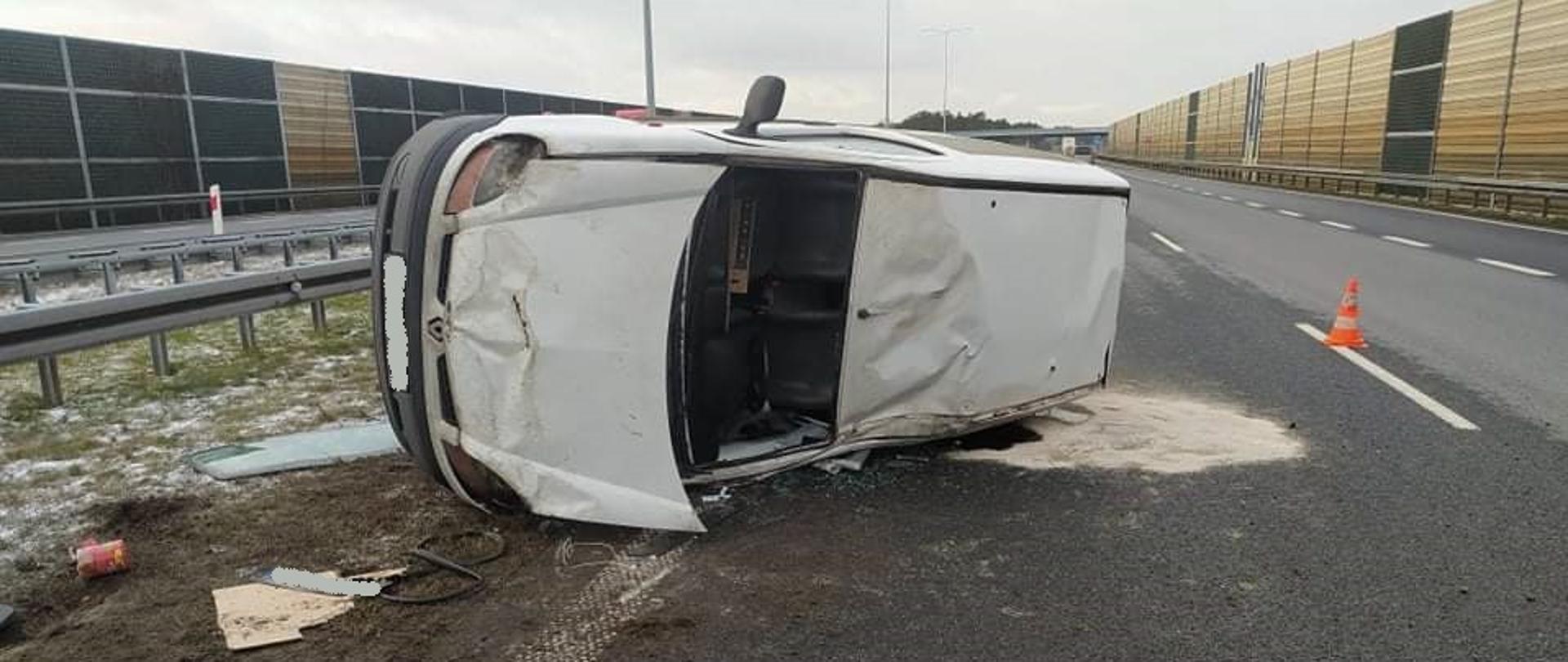 Zdjęcie przedstawia samochód osobowy. po wypadku. Samochód leży na lewym boku.