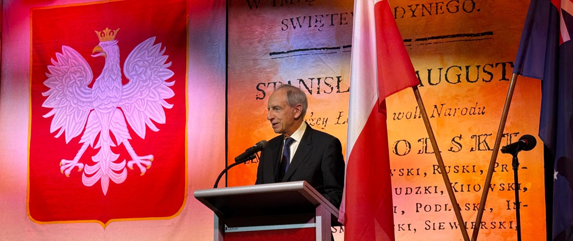 The Minister speaks on stage, with the Polish coat of arms in the background.