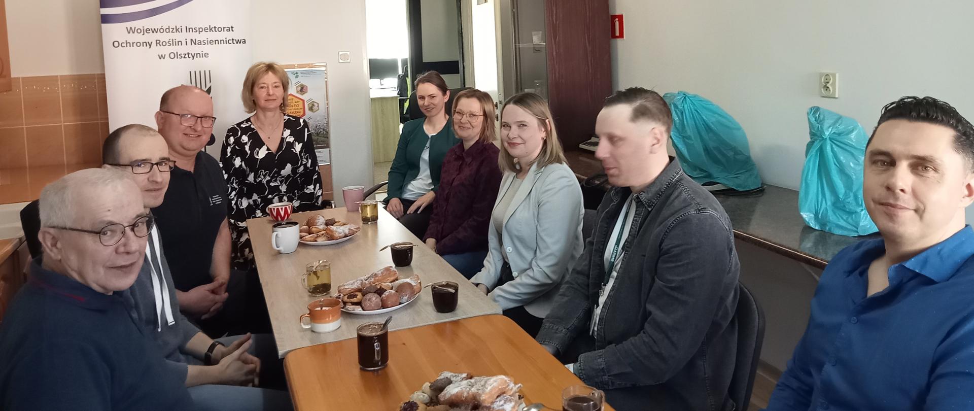 grupa osób siedzi po obu stronach podłużnego stołu pozując do zdjęcia. 