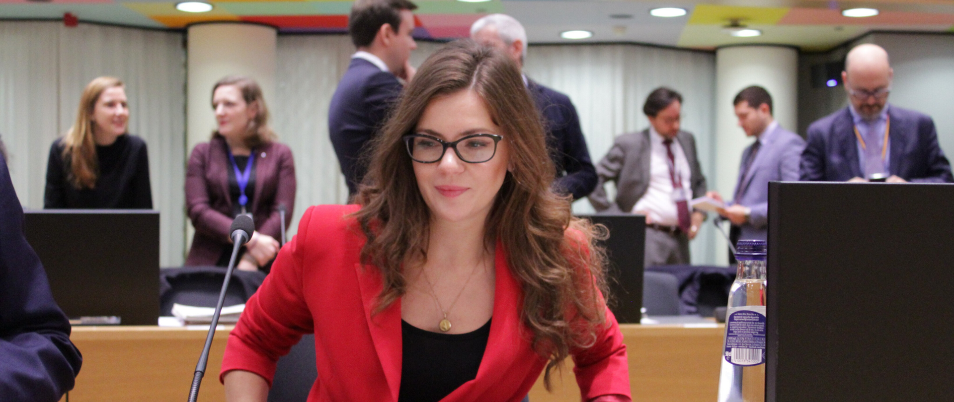 Minister Wanda Buk siada przy stole w sali obrad. W tle inni uczestnicy spotkania