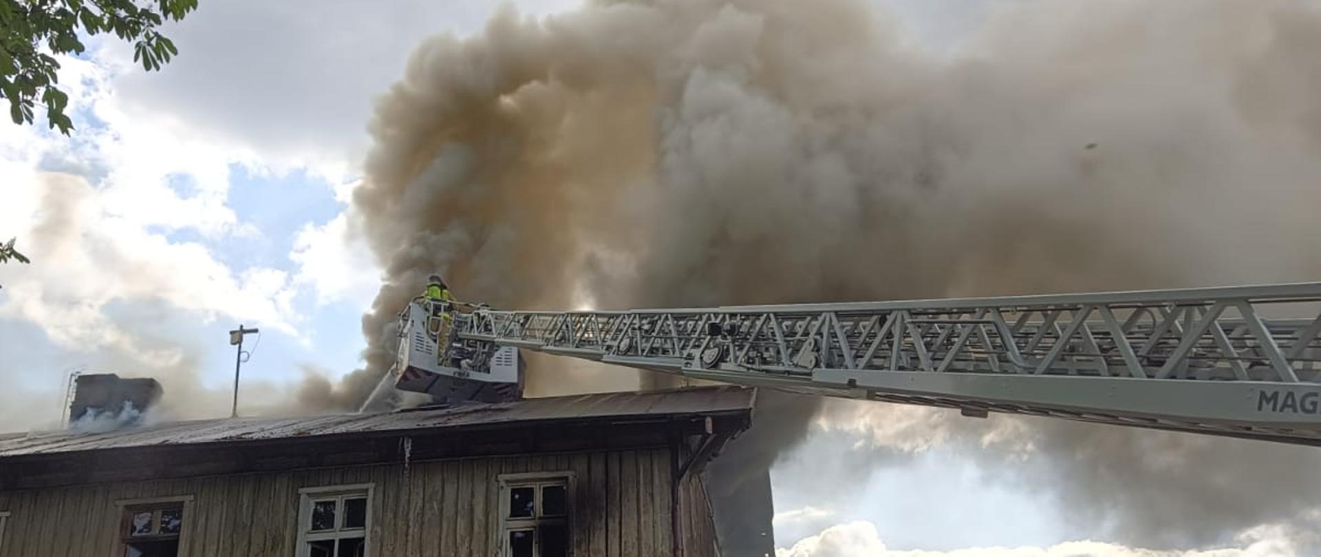 Strażacy na drabinie gaszą dach budynku mieszkalnego 