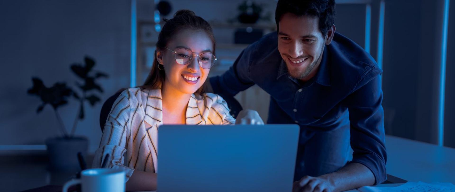 Dwoje ludzi, kobieta i mężczyzna przeglądają komputer z uśmiechem 