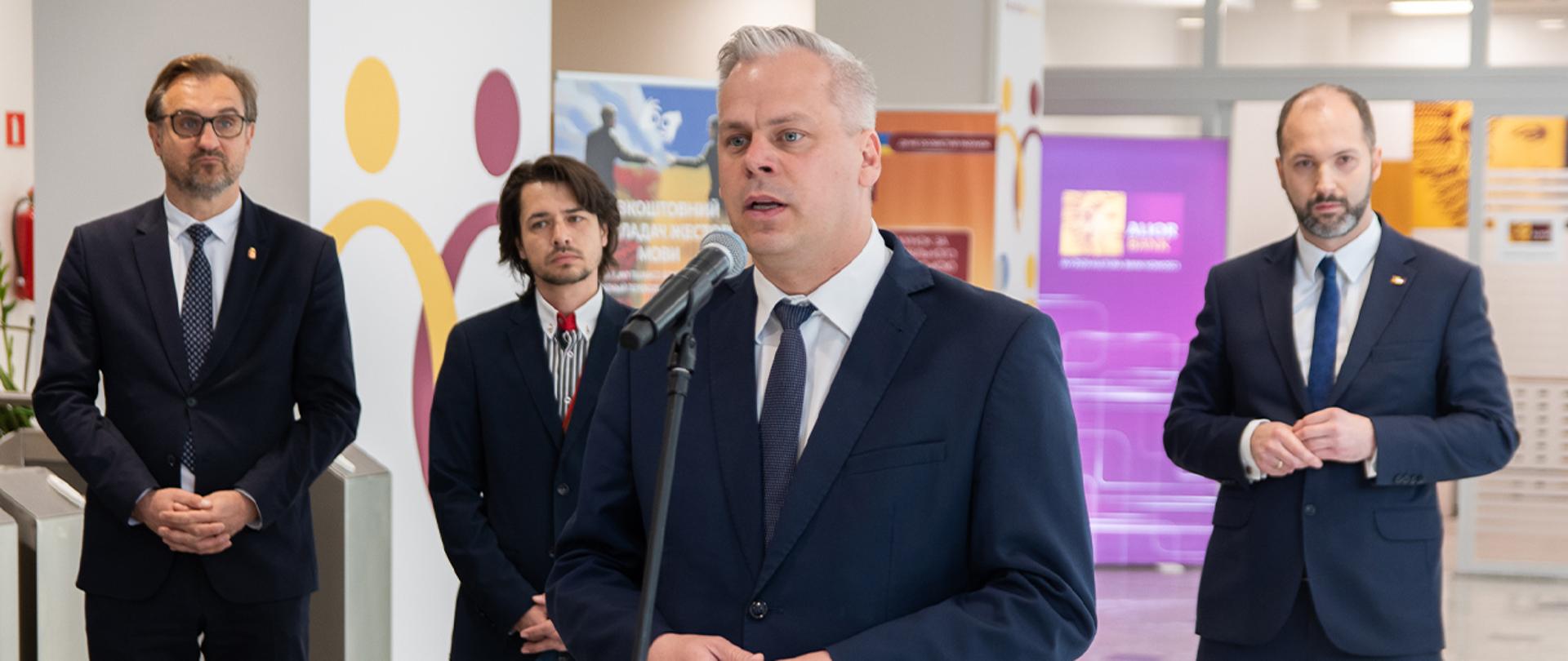 Wiceminister Karol Rabenda stoi przy mikrofonie. W tle stoi trzech mężczyzn.