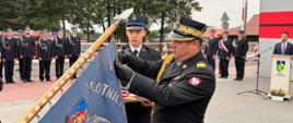 „Ceremonia dekoracji sztandaru jednostki OSP Morzyczyn-Włóki. Komendant Wojewódzki PSP nadbryg. Artur Gonera w asyście strażaka przypina odznaczenie do płata sztandaru. W tle zgromadzeni strażacy i zaproszeni goście.”