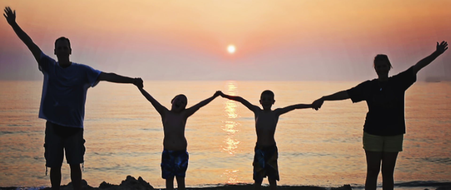 rodzice z dwójką dzieci stoją na plaży na tle zachodzącego słońca