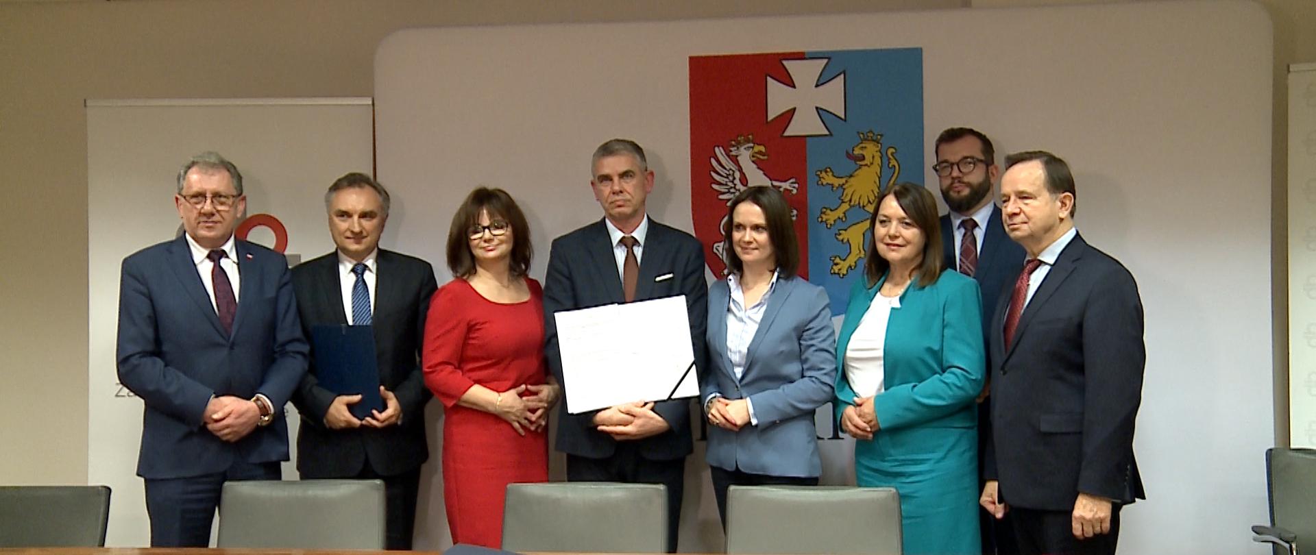 Na zdjęciu grupa ludzi pozuje z podpisaną umową