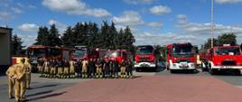 na placu komendy stoją ustawione samochody pożarnicze a przed nimi strażacy czekający na odprawę