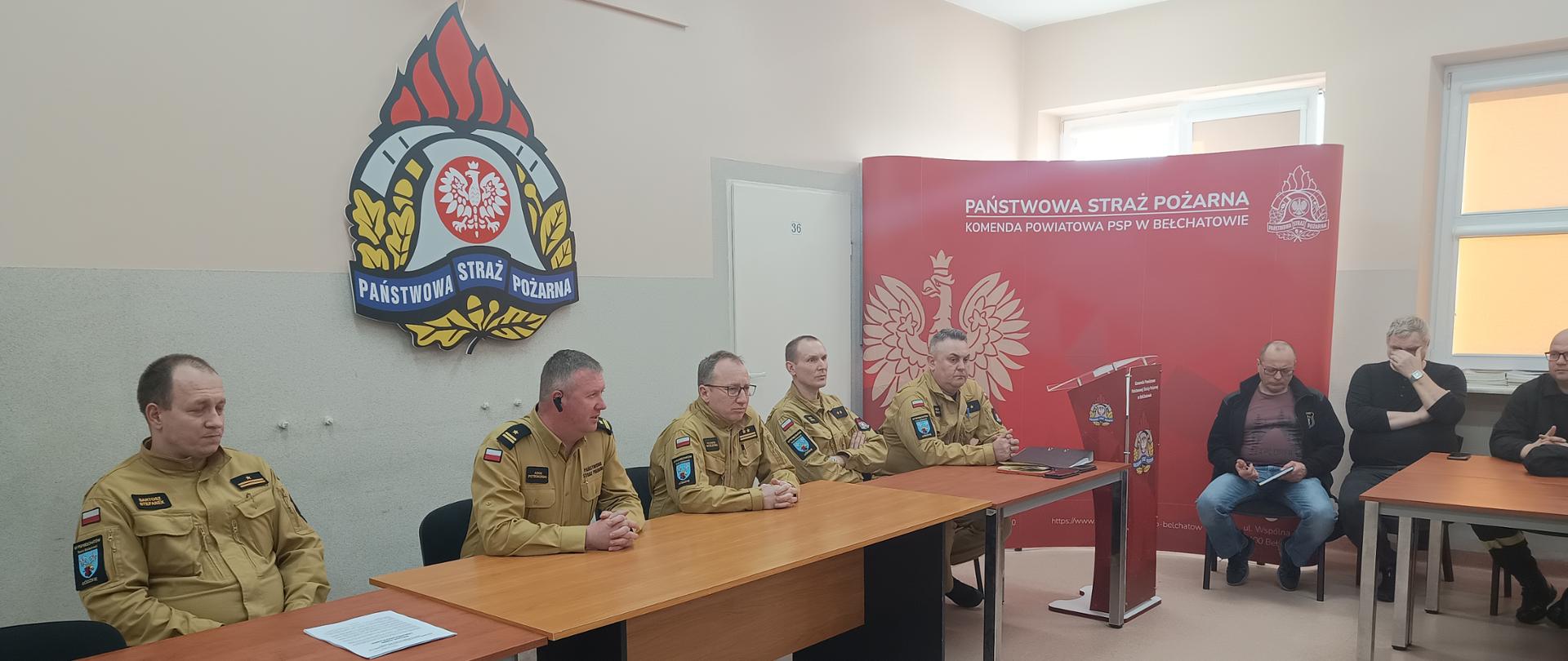 na zdjęciu widzimy strażaków w mundurach służbowych oraz strażaków OSP w tle logo straży i czerwony bilbord straży pożarnej